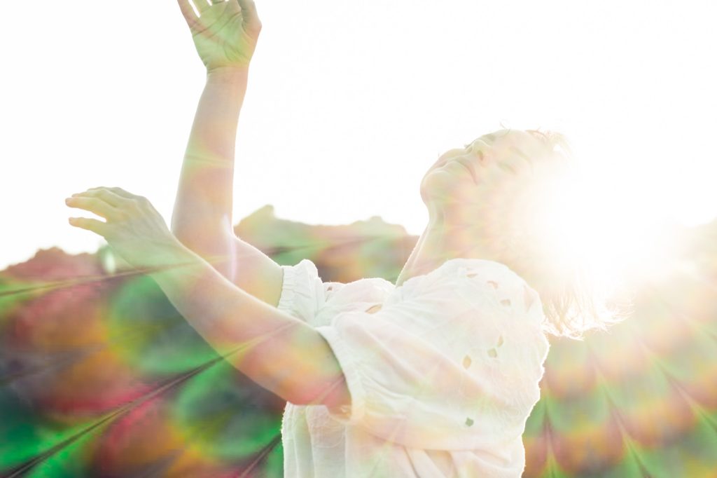 A woman reaching her arms toward the sun, double-exposed with leaves