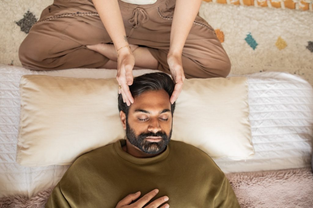 A client lies with eyes closed receiving Reiki, one hand resting on the heart while the practitioner cradles the head, in the Word of Mouth healing room in Los Angeles.